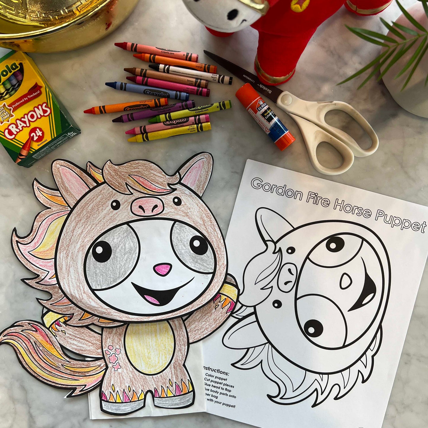 Gordon & Li Li Year of the Fire Horse Puppet Craft, crayons, scissors, and a plush toy on a marble surface.